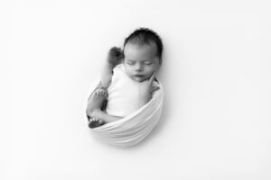 Newborn baby curled up with finger on cheek photographed by newborn photographer Melanie East