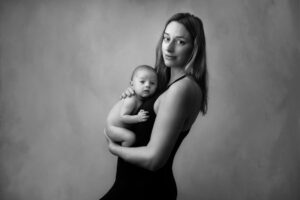 A mother holding her baby to her chest. Mother and baby are looking at the camera. The image is tender and emotional and photographed in black and white. Mother and baby photography by leading newborn photographer Melanie East in Bristol