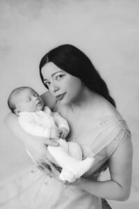 A tender image of a mother and baby. Baby is held by mother and the mother is nestling into his face. Baby is wearing a white plain babygrow. Shot in black and white.