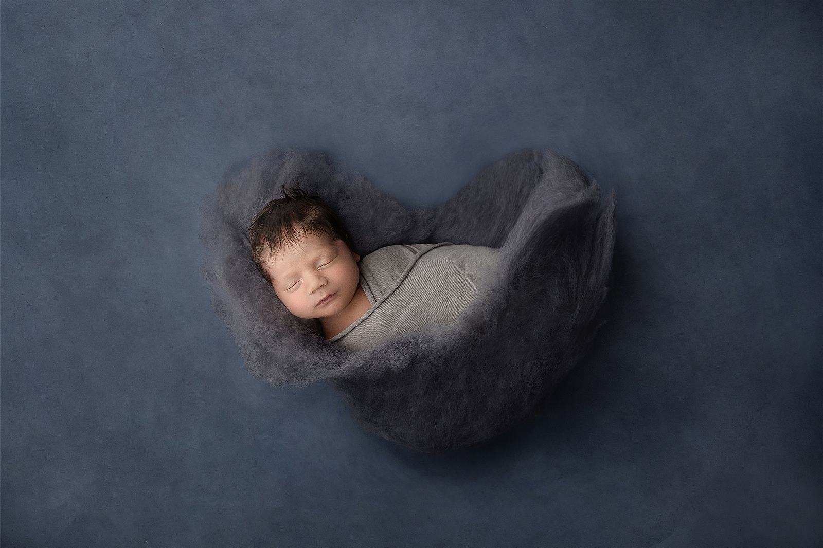 Newborn baby wrapped up and nestled in a cosy soft heart photographed by newborn photography trainer Melanie East