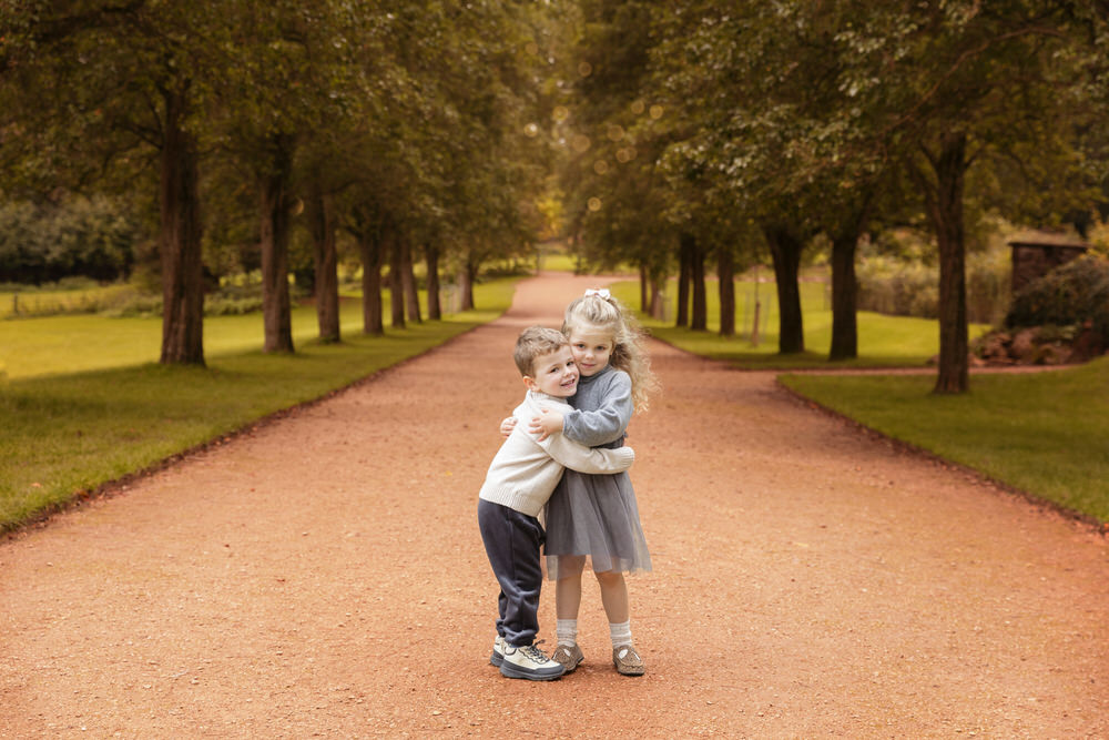 Twins one boy one girl aged about 5 hugging in a tree lined avenue. photographed by outdoor portrait photographer Melanie East in Bristol